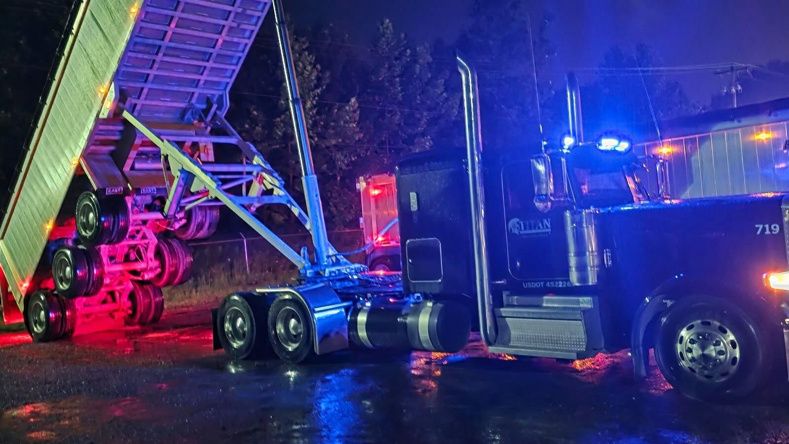 Titan Trucking 719 raising its end dump at night under blue lights