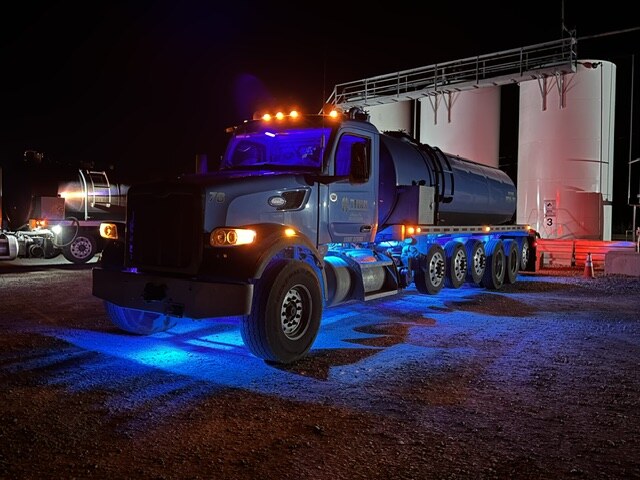 Titan water truck glowing with blue underglow at a tank battery at night