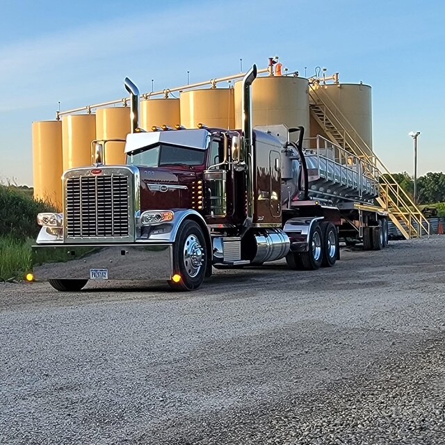 Maroon Titan Peterbilt with vacuum trailer in front of storage tanks